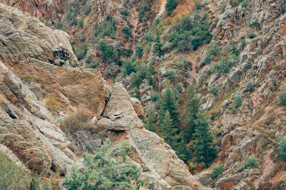 Hunter wearing A-Tacs camo aiming an X-Bolt rifle on a cliff